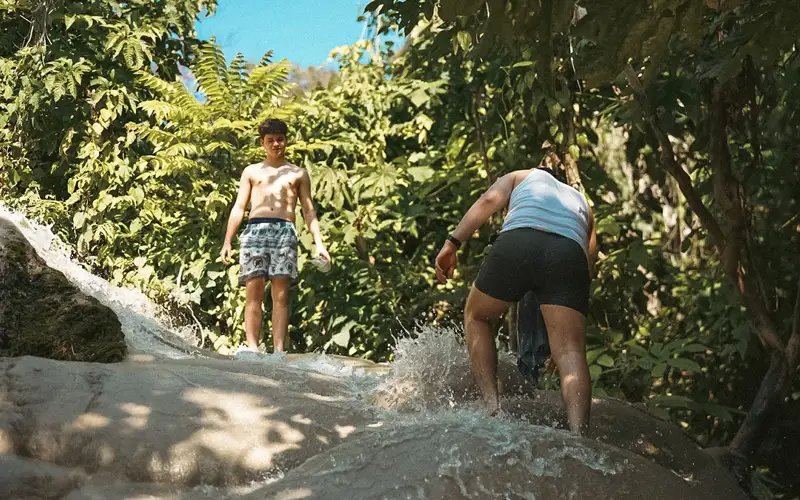 Travelers climbing up the Sticky Waterfall limestone surface with water flowing down. Travelers climbing up the Sticky Waterfall limestone surface with water flowing down.
