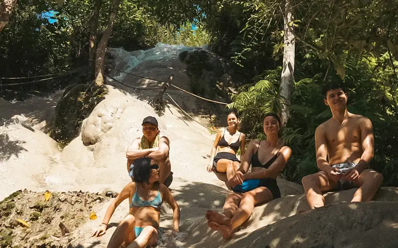 Small group sitting on limestone rocks at Sticky Waterfall with jungle trees and cascades behind. Small group sitting on limestone rocks at Sticky Waterfall with jungle trees and cascades behind.