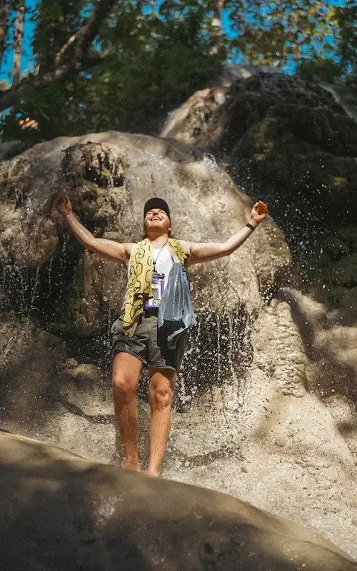 Traveler standing under the Sticky Waterfall stream with water splashing over limestone rocks in Chiang Mai. Traveler standing under the Sticky Waterfall stream with water splashing over limestone rocks in Chiang Mai.