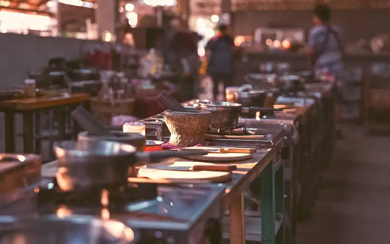 Row of prepared cooking stations with woks, mortar and pestle, and ingredients set up for a Thai cooking class. Row of prepared cooking stations with woks, mortar and pestle, and ingredients set up for a Thai cooking class.