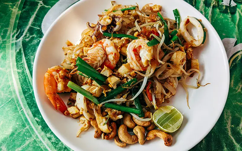 Close-up of a finished Pad Thai dish with shrimp, cashews, green onions, and lime served on a plate. Close-up of a finished Pad Thai dish with shrimp, cashews, green onions, and lime served on a plate.